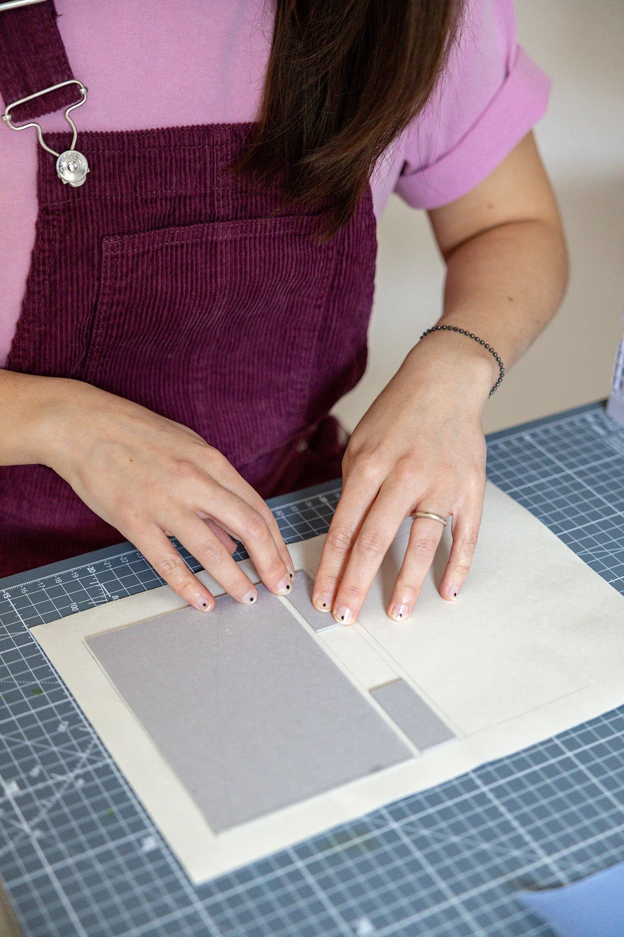 Mani al lavoro in fase di incollaggio del cartone grigio pressato su tela da legatoria su piano di lavoro.