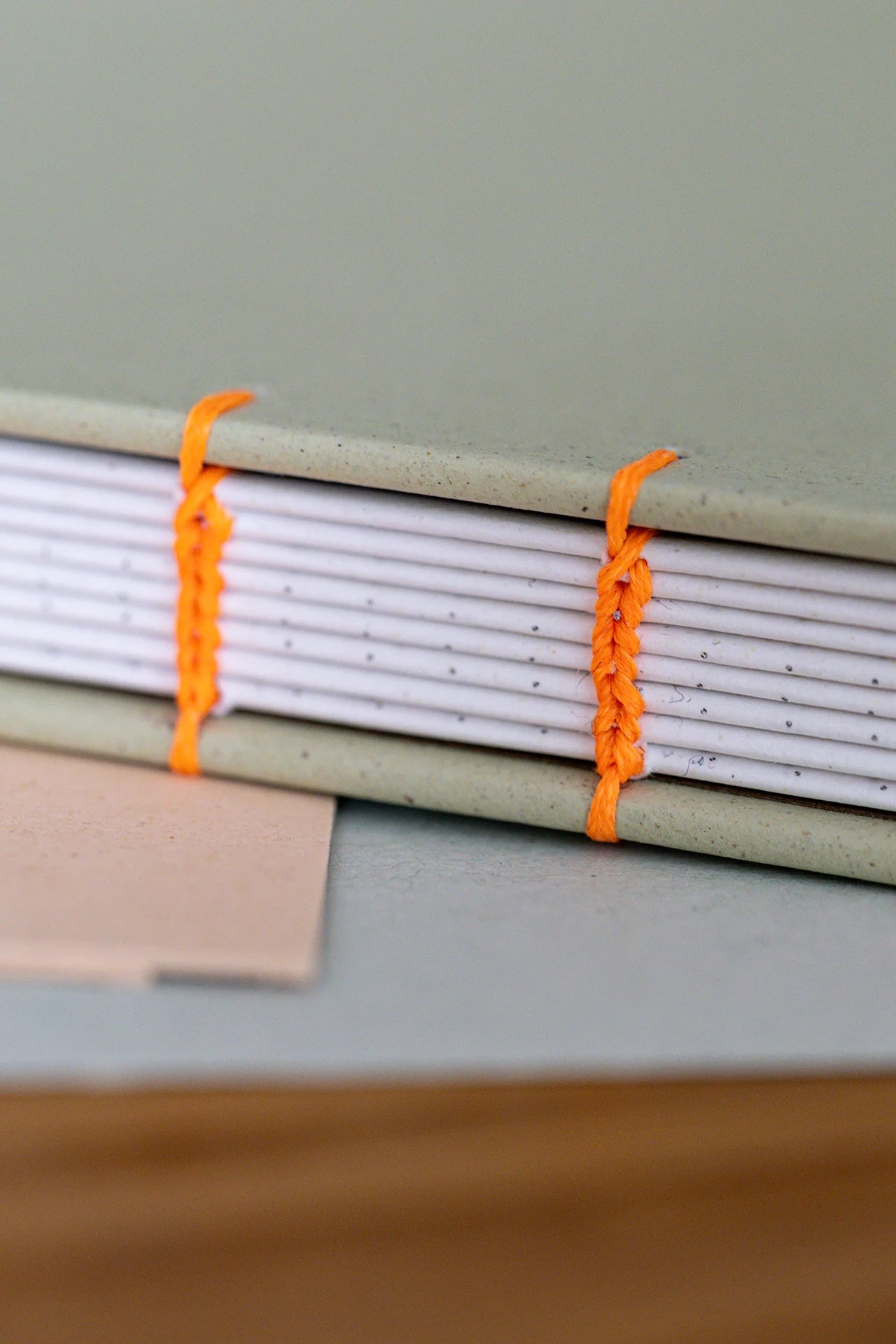 Dettaglio legatura artigianale copta e legatura a fiocco in filo arancione fluo che uniscono fascicoli in carta riciclata di qualità dotted regalo unico fatto a mano.