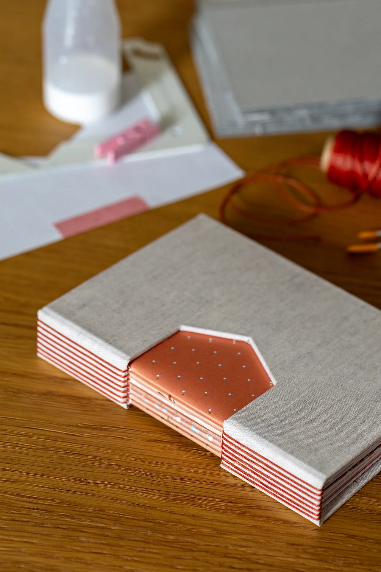 Taccuino sartoriale con tonalità beige, arancioni e corten, rilegato a mano con tecnica Buttonhole, in copertina intaglio geometrico.